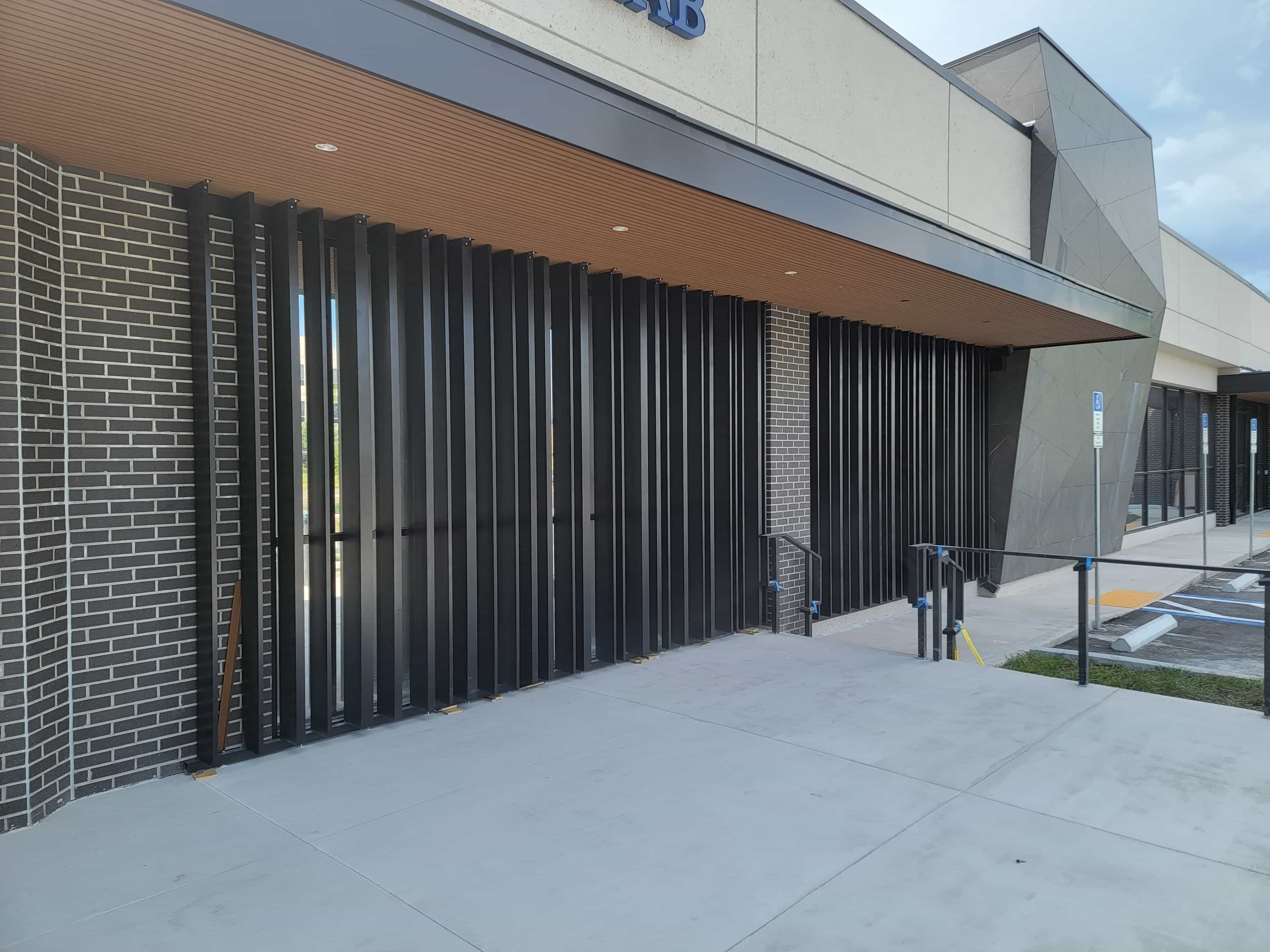 Vertical steel louvre screen mounted along a brick commercial facade