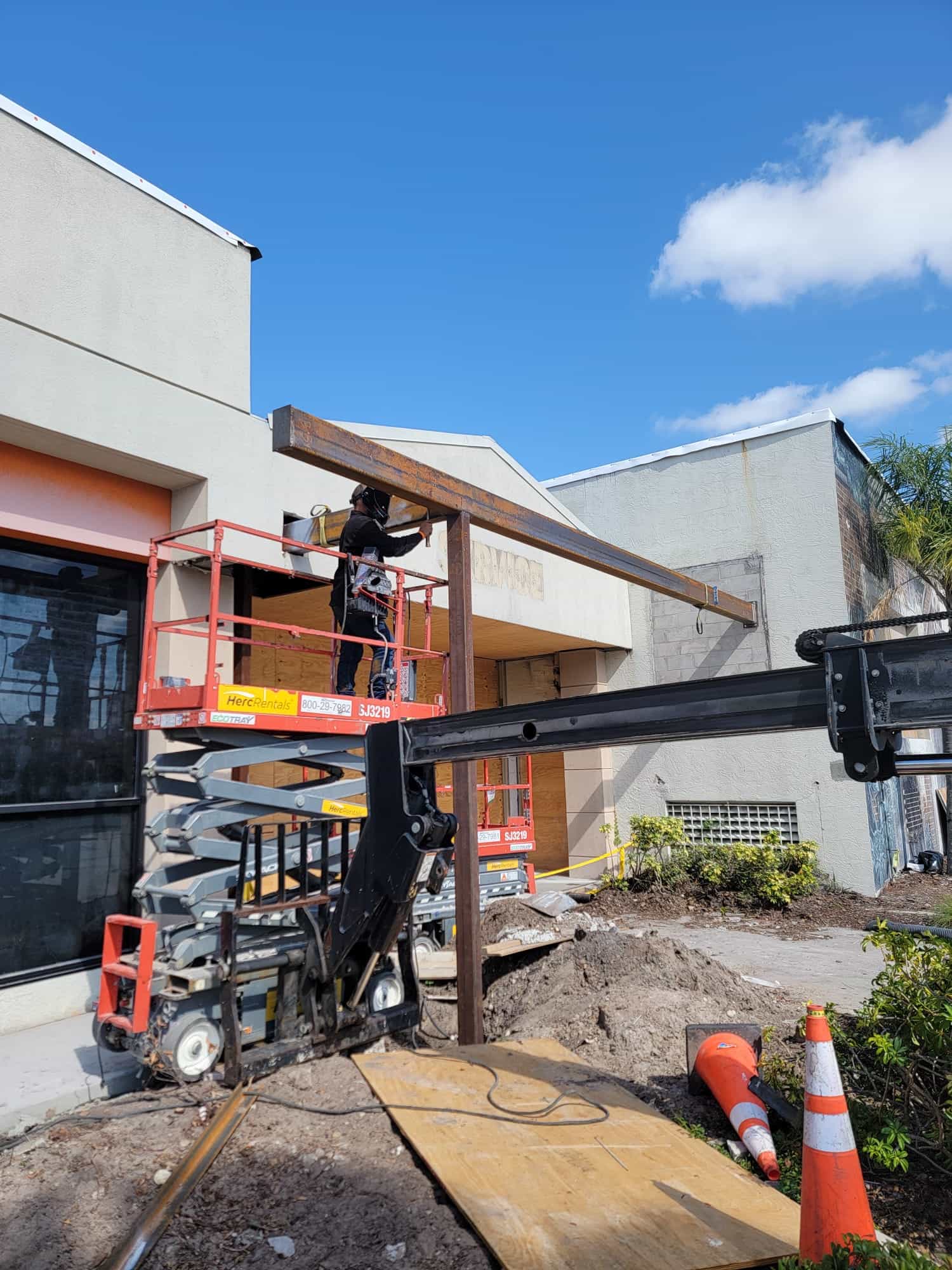 Welder on a scissor lift installing a structural steel canopy beam on a commercial storefront